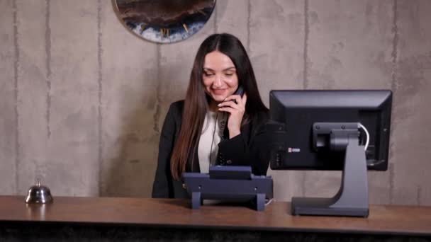 ホテル受付係 ベル付きのモダンなホテルのフロントデスク ホテルのカウンターに立って電話で話す幸せな女性受付係 — ストック動画