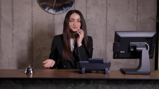 ホテル受付係 ベル付きのモダンなホテルのフロントデスク ホテルのカウンターに立って電話で話す幸せな女性受付係 — ストック動画