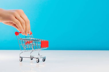 İş ve e-ticaret kavramı. Stüdyoda mavi bir arka planda dururken boş bir alışveriş arabasını iten parmakları kullanarak yakın plan. Yan görüş. Metin için boşluk