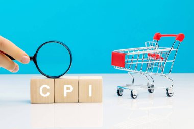 CPI - Consumer Price Index symbol.Letter block in word CPI abbreviation of consumer price index with a magnifying glass in woman's hand near empty shopping cart on blue background. Business and CPI, consumer price index concept