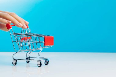 İş ve e-ticaret kavramı. Stüdyoda mavi bir arka planda dururken boş bir alışveriş arabasını iten parmakları kullanarak yakın plan. Yan görüş. Metin için boşluk