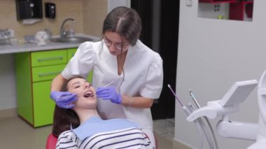 Kadın dişçi, genç bayan hasta için tedavi görüyor, diş aletleri tutuyor, lastik eldiven takıyor. Modern diş sağlığı kliniği kavramı