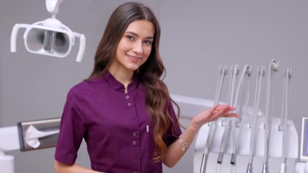 一位年轻漂亮的女牙医正站在办公室的牙椅旁边 用手摆姿势 — 图库视频影像