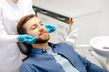 Modern klinikte dişçi koltuğunda oturup gülümseyen mutlu bir adamın portresi. Profesyonel dişçide diş tedavisinden hoşlanan hasta.