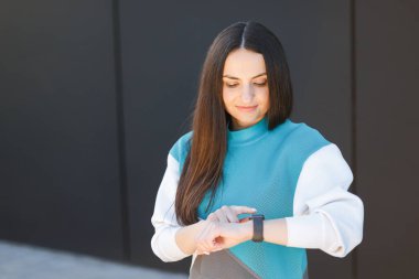 Kadın ellerindeki nabzı ölçmek için akıllı bir saat kullanıyor. Sokakta spor yapan bir kadın. Fitness ve sağlıklı bir yaşam tarzı.