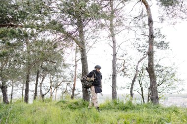 Üniformalı ve taktik yelekli genç asker ormanda çalışıyor ve geçici bir orman üssünde harekete geçmeye hazırlanıyor. Bir adam bölgeyi mayınlardan arındırmak için çalışır..