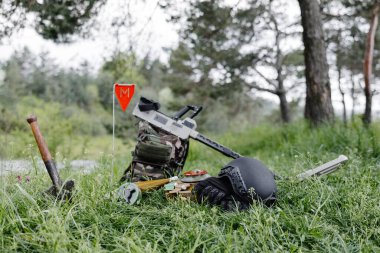 Explosive devices and a metal detector lie on the background of a forest massif. Equipment for demining the territory. clipart