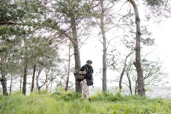 stock image Young soldier in uniforms and tactical vest works in the forest and prepares for action at a temporary forest base. A man does in the work of demining the territory.