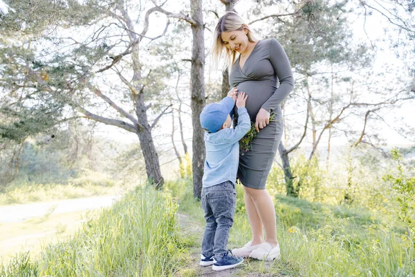 可爱的男孩在森林里摸妈妈怀孕的肚子 怀孕的母亲和她的小儿子一起散步 一起度过有趣的时光 — 图库照片
