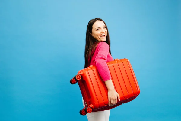 Stock image Portrait of happy young woman running and holding baggage isolated on blue background.