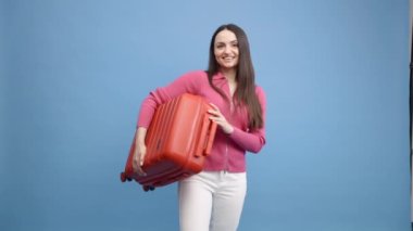Mavi arka planda koşan ve bavulları taşıyan mutlu genç bir kadının portresi.