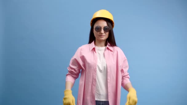 戴黄色头盔和手套的妇女在蓝色工作室背景下指指点点和做手势 — 图库视频影像