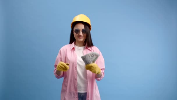 戴黄盔的年轻女子带着现金钞票 背景是蓝色的 修理家园的概念 — 图库视频影像