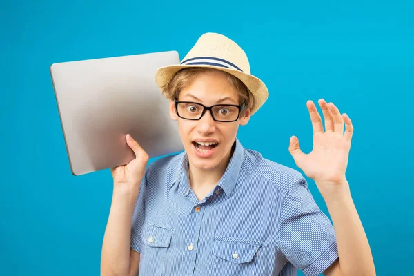 Waist up portrait view of the funny businessman teen holding laptop in hands. Indoor studio shot isolated on blue background