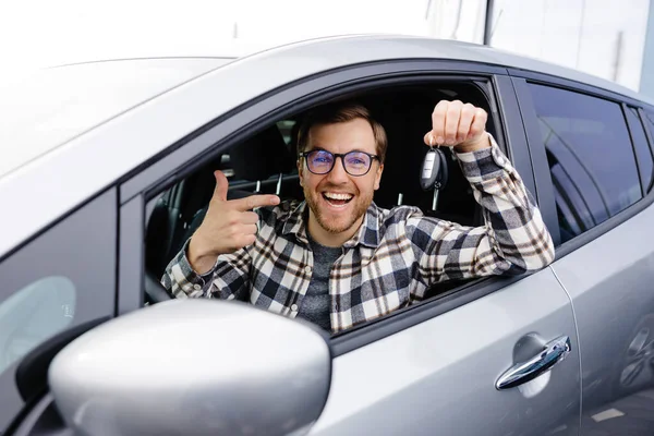 Excited young man showing a car key, sitting inside his new vehicle.