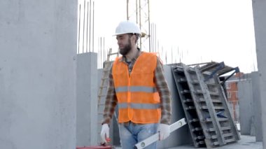İnşaatçı, miğfer ve yelek giyen ustabaşı inşaat halindeki bir binada iş yerinde çalışıyor.