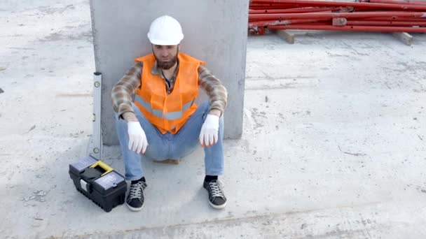 工具箱と定規の隣の建物の職場で休むために座っているビルダー修理工 安全ヘルメットとベストのフォアマン — ストック動画