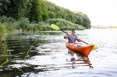 Nehirde kano yapıyorum. Genç beyaz bir adam kano ve kürek içinde oturur. Su eğlencesi konsepti.