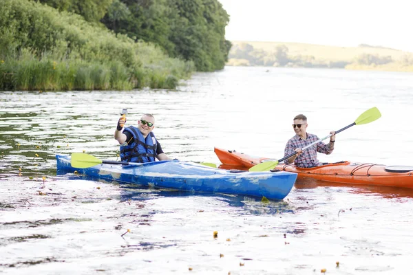 在河里划船 两个年轻人坐在皮划艇上 拿着便携式相机自拍 水娱乐的概念 — 图库照片