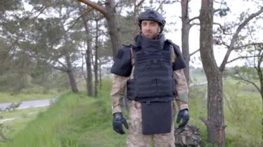 Üniformalı ve taktik yelekli genç asker ormanda çalışıyor ve geçici bir orman üssünde harekete geçmeye hazırlanıyor. Bir adam bölgeyi mayınlardan arındırmak için çalışır.