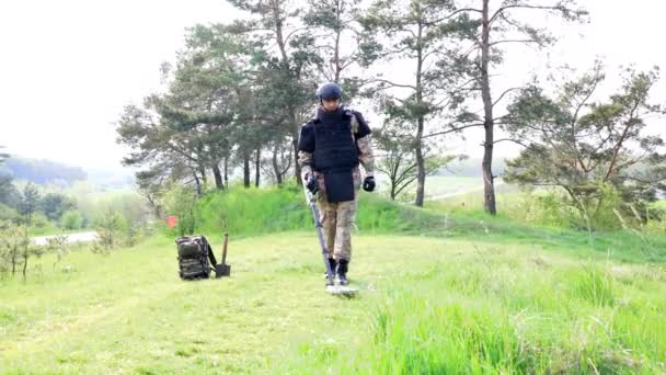 軍の制服と防弾チョッキを着た男が金属探知機で森の中で働いている 掃海艇が領域を地雷除去する作業を行う — ストック動画