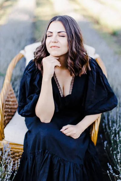 迷人的年轻女子穿着黑色衣服坐在被薰衣草场包围的椅子上 — 图库照片