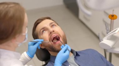 A handsome man is sitting in a chair at a woman's appointment at the dentist's office