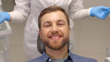 Modern klinikte dişçi koltuğunda oturan ve gülümseyen mutlu adam. Profesyonel dişçide diş tedavisinden hoşlanan hasta