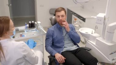 Sad man sitting in dental chair suffering from acute tooth pain, rubbing his cheek, close up