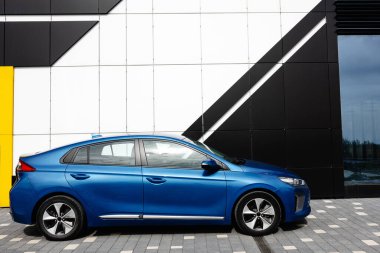 Modern binaya park etmiş elektrikli bir araba. Elektrikli araba şarj sırasında caddedeki otoparkta..