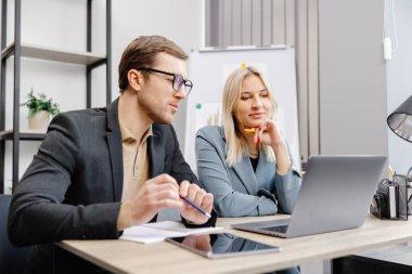 Ofiste dizüstü bilgisayar kullanan neşeli iş adamları. Modern bir çalışma alanında birlikte çalışırken gülümseyen genç girişimciler. Masada birlikte oturan iki genç iş adamı.