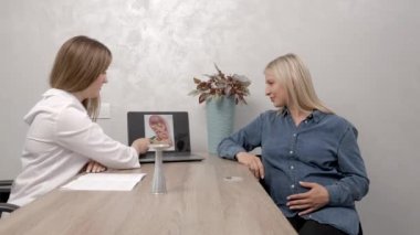 Genç hamile bir kadın klinikteki jinekoloğunu ziyaret ediyor. Sandalyeye oturup doktoruyla konuşuyor.