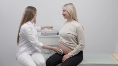 Doktor hamile bir kadını fetal monitörle fetüsün kalp atışlarını kontrol etmeye hazırlıyor.