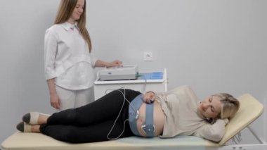 Doktor hamile bir kadını fetal monitörle fetüsün kalp atışlarını kontrol etmeye hazırlıyor.
