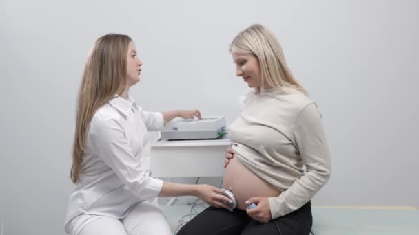 医師は胎児のモニタリングによって胎児のハートビートをチェックするための妊婦を準備 — ストック動画