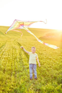 Elinde uçurtmayla tarlada koşan küçük bir çocuk.