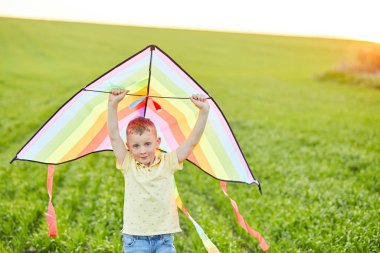 Elinde uçurtmayla tarlada koşan küçük bir çocuk.
