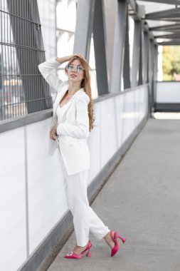 Stylish adorable pretty woman with wavy hair wearing white stylish suit and sunglasses standing and having fun in the street.