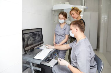 Genç dişçilerden oluşan bir ekip iyi donanımlı bir ofiste çalışıyor. Diş hekimleri hastanın çenesinin fotoğrafını çeker