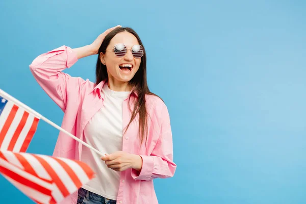 年轻快乐的女人穿着休闲装 举着美国国旗 凝视着蓝色背景的相机 — 图库照片