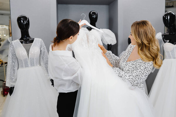 Young woman choosing wedding dress in salon. The bride-to-be came to a wedding dress salon to buy a dress.