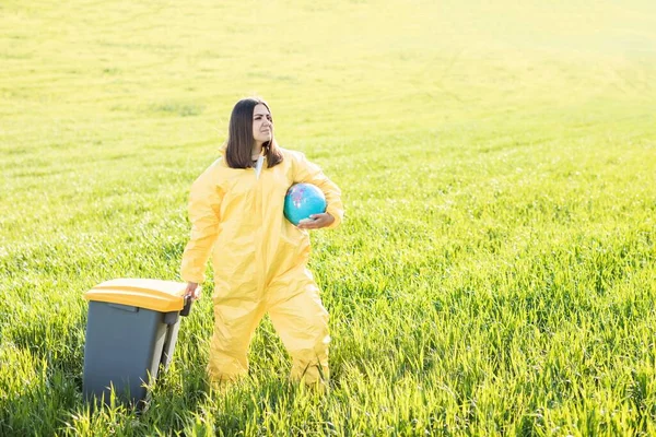 Woman Yellow Protective Suit Stands Middle Green Field Holding Globe — Stock Photo, Image