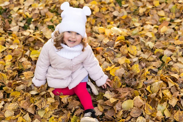 stock image A cute pretty girl is running in the park in the middle of autumn leaves and smiling