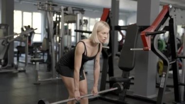 Sportif genç fitness kadını spor salonunda halterle kaldırma egzersizi yapıyor.