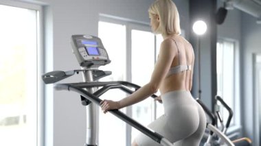 Spor giyim bölümünde spor salonunda çalışan genç bir kadın. Merdiven simülatöründe çalışıyor.