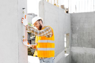 İnşaatçı-tamirci, ustabaşı, koruyucu bir miğferle beton bir binanın merdivenlerini kontrol eder..