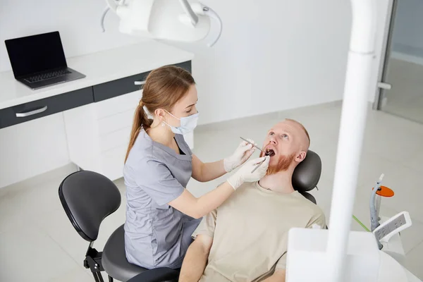 Klinikte Orta Yaşlı Bir Adamın Yanında Duran Genç Kadın Dişçinin — Stok fotoğraf