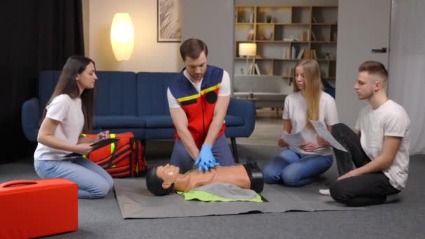 グループトレーニングの前にダミーと応急処置の心臓の圧縮をする準備をしている若い男のインストラクター屋内 — ストック動画