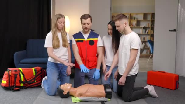 屋内グループトレーニング中にダミーと応急処置の心の圧縮を作るのを助ける若い男のインストラクター — ストック動画