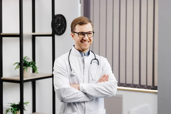 Smiling doctor posing with arms crossed in the office. Man is wearing a stethoscope and glasses. Medical staff on the workplace.